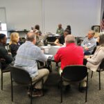 group of people sitting around a table conversing in a conference room