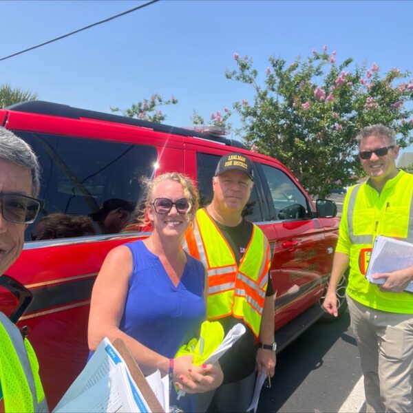 Men and woman with neon vests pose in front of a red car.