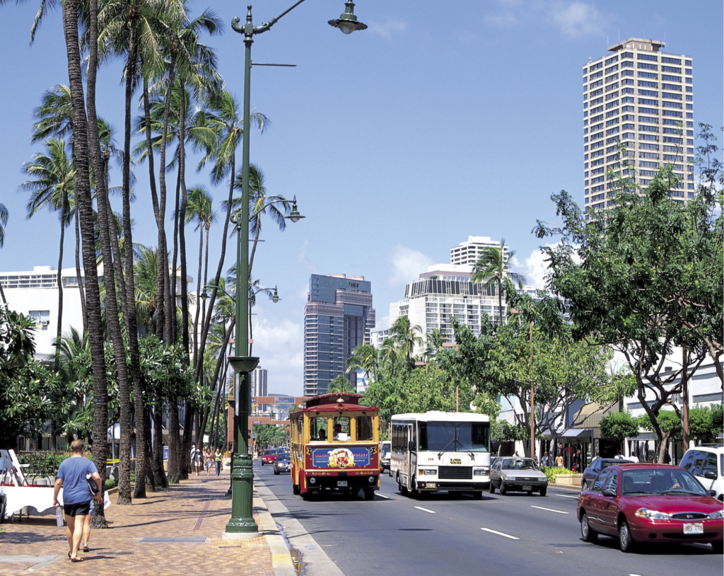 a street in a tropical location with buses, cars, and pedestrians