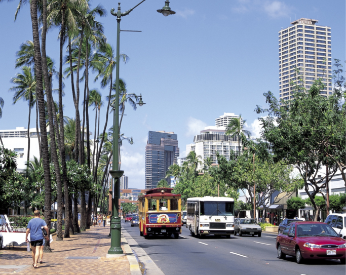 a street in a tropical location with buses, cars, and pedestrians