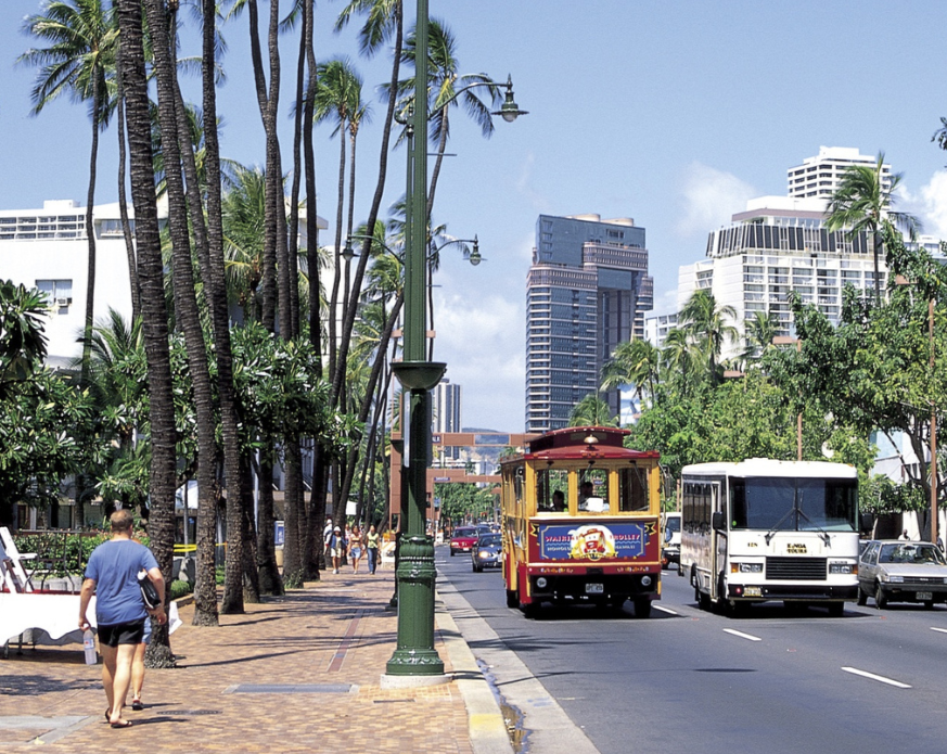 street in tropical location with trolley, buses, cars, and pedestrians