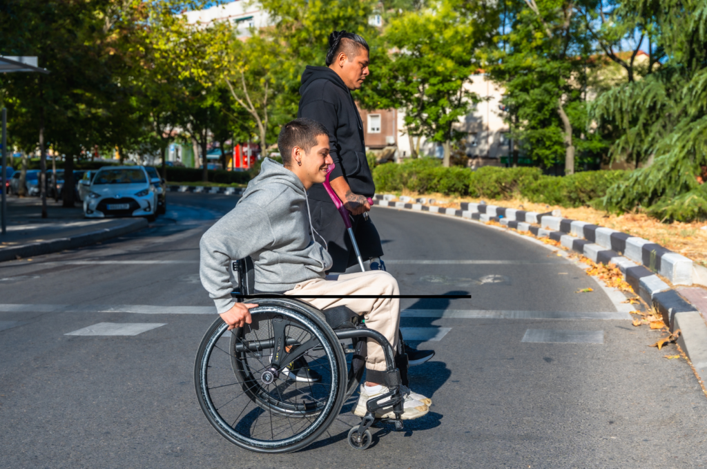 young man in wheel chair crossing street with another man