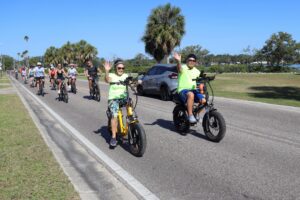 people biking down a paved road and waving
